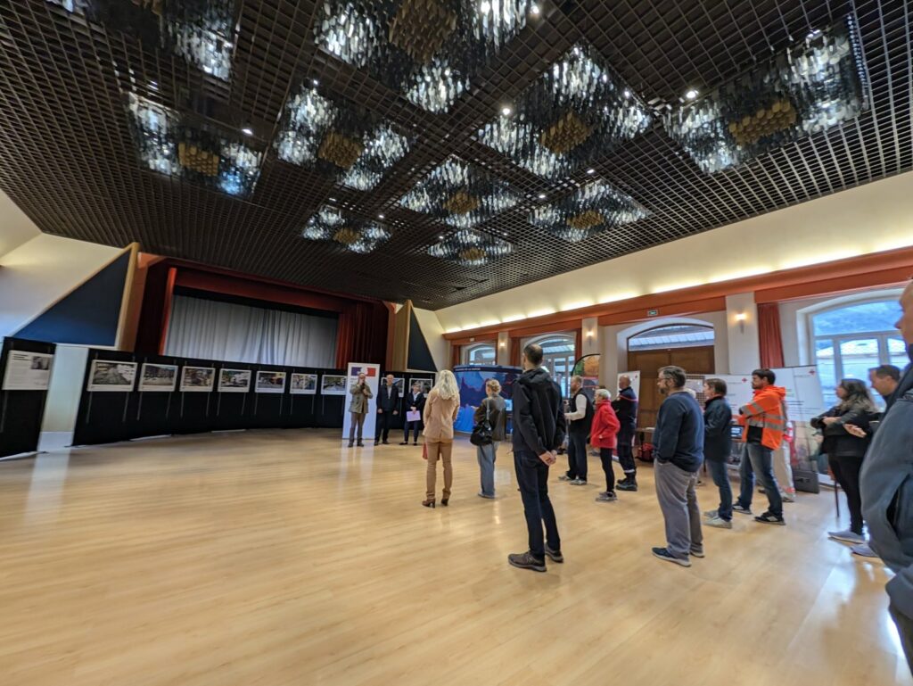 Public dans la salle des fêtes de Fourneaux devant les panneaux de l'exposition Souvenirs majeurs du Charmaix